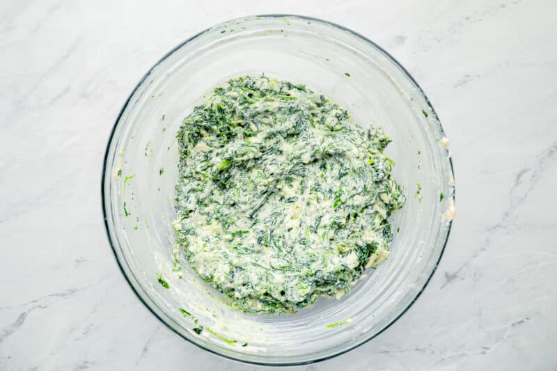spinach and cheese added to cream cheese mixture in a glass bowl.