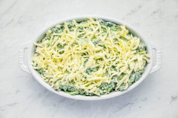 overhead view of shredded cheese sprinkled over bacon spinach dip in an oval baking dish.