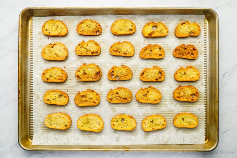 25 toasted slices of french bread on a baking sheet.