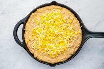cheese sprinkled over unbaked cheesy bean dip in a cast iron skillet.