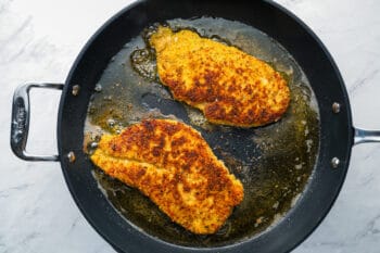 2 pan fried breaded chicken breasts in a cast iron skillet.