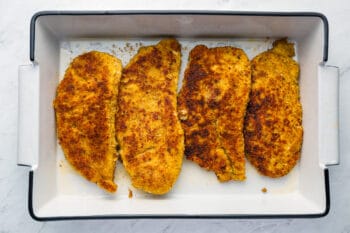 4 pan fried breaded chicken breasts in a rectangular baking pan.