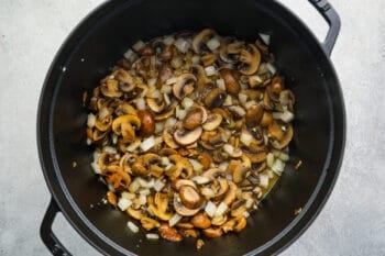 onions and garlic added to mushrooms in a dutch oven.