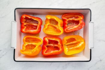 3 partially cooked halved bell peppers cut side up in a baking pan.