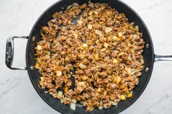 seasonings added to beef and onions in a frying pan.