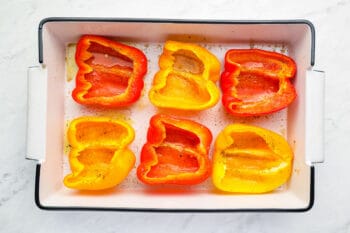 3 halved bell peppers cut side up in a baking pan.