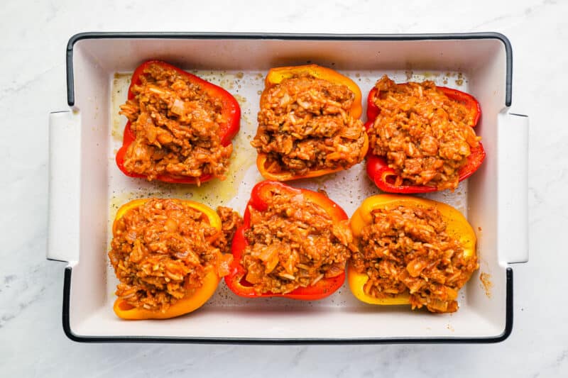 6 bell pepper halves stuffed with ground beef and rice mixture in a white rectangular baking pan.