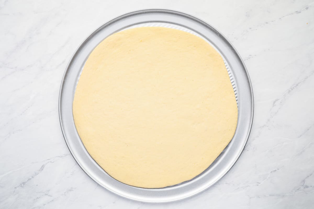 Rolled out pizza dough on a pizza pan.