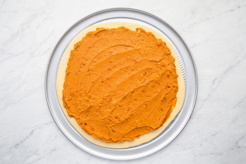 refried beans spread over pizza dough on a pizza pan.