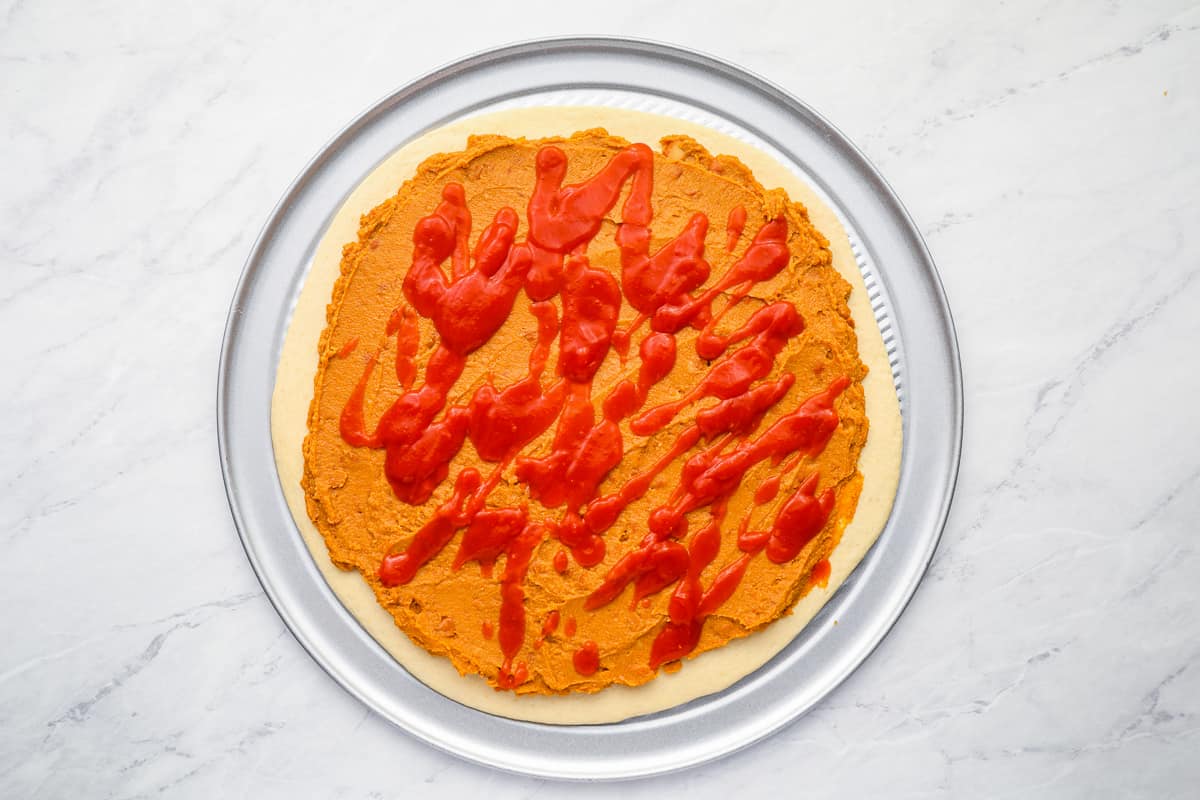 Taco sauce drizzled over refried beans on pizza dough.