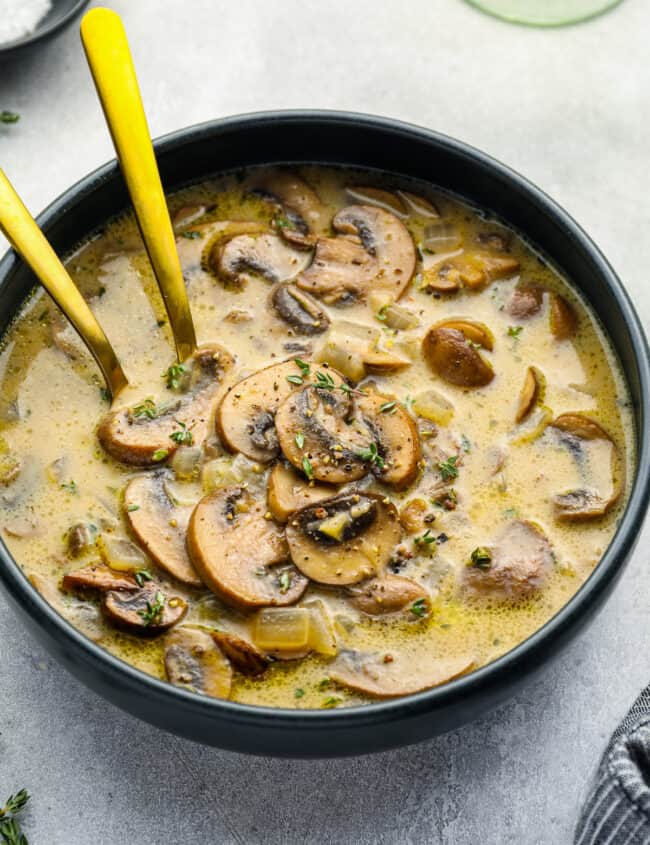 mushroom soup in a black bowl with 2 spoons.