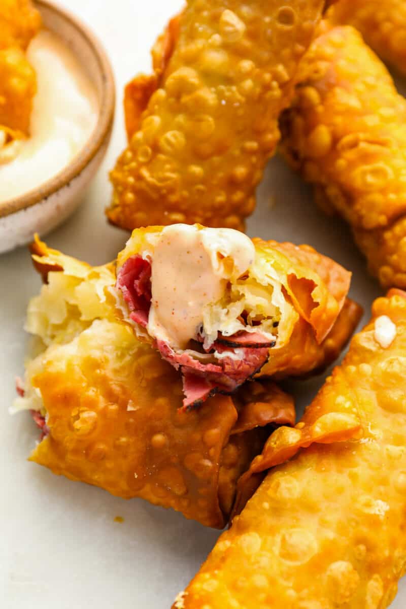 close up of a broken reuben egg roll dipped in russian dressing perched atop more egg rolls.