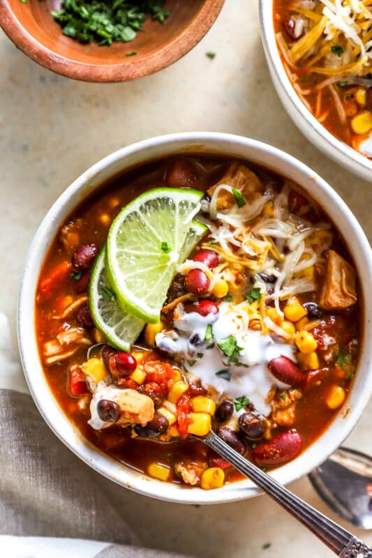 overhead view of a bowl of 7 can soup with lime wedges, cheese, and a spoon.