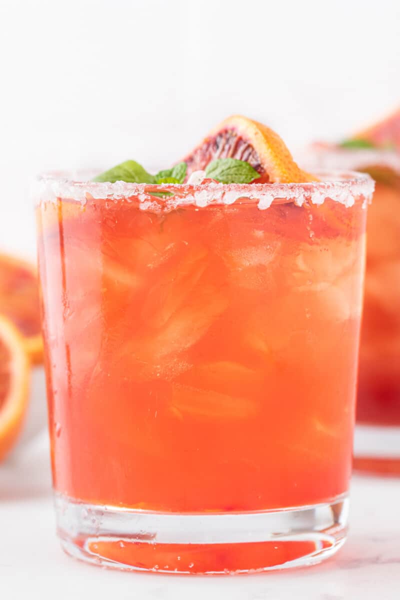 close up side view of a blood orange margarita garnished with a blood orange slice and mint leaves.