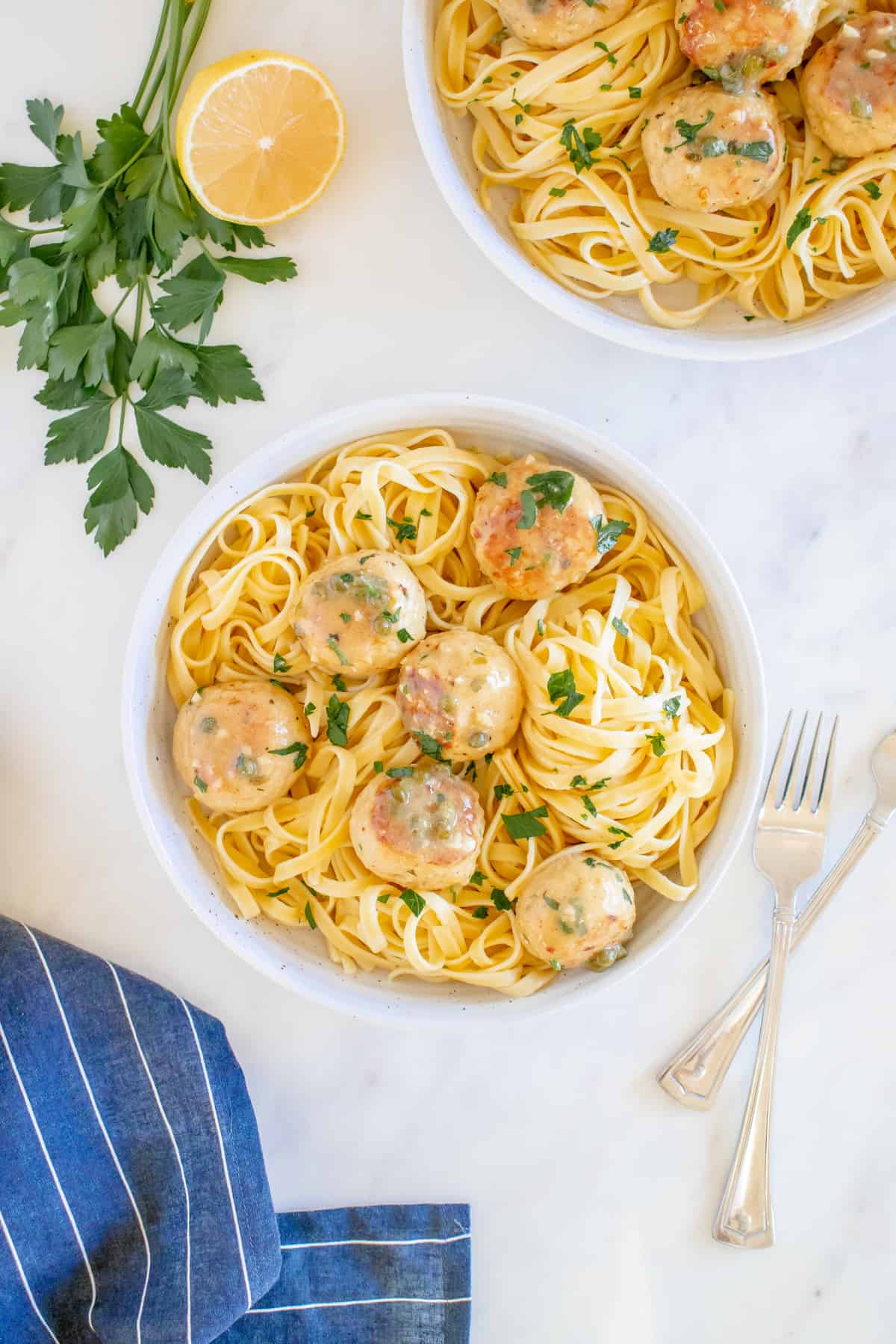 overhead view of 6 chicken piccata meatballs on a bed of fettuccini in a white bowl.