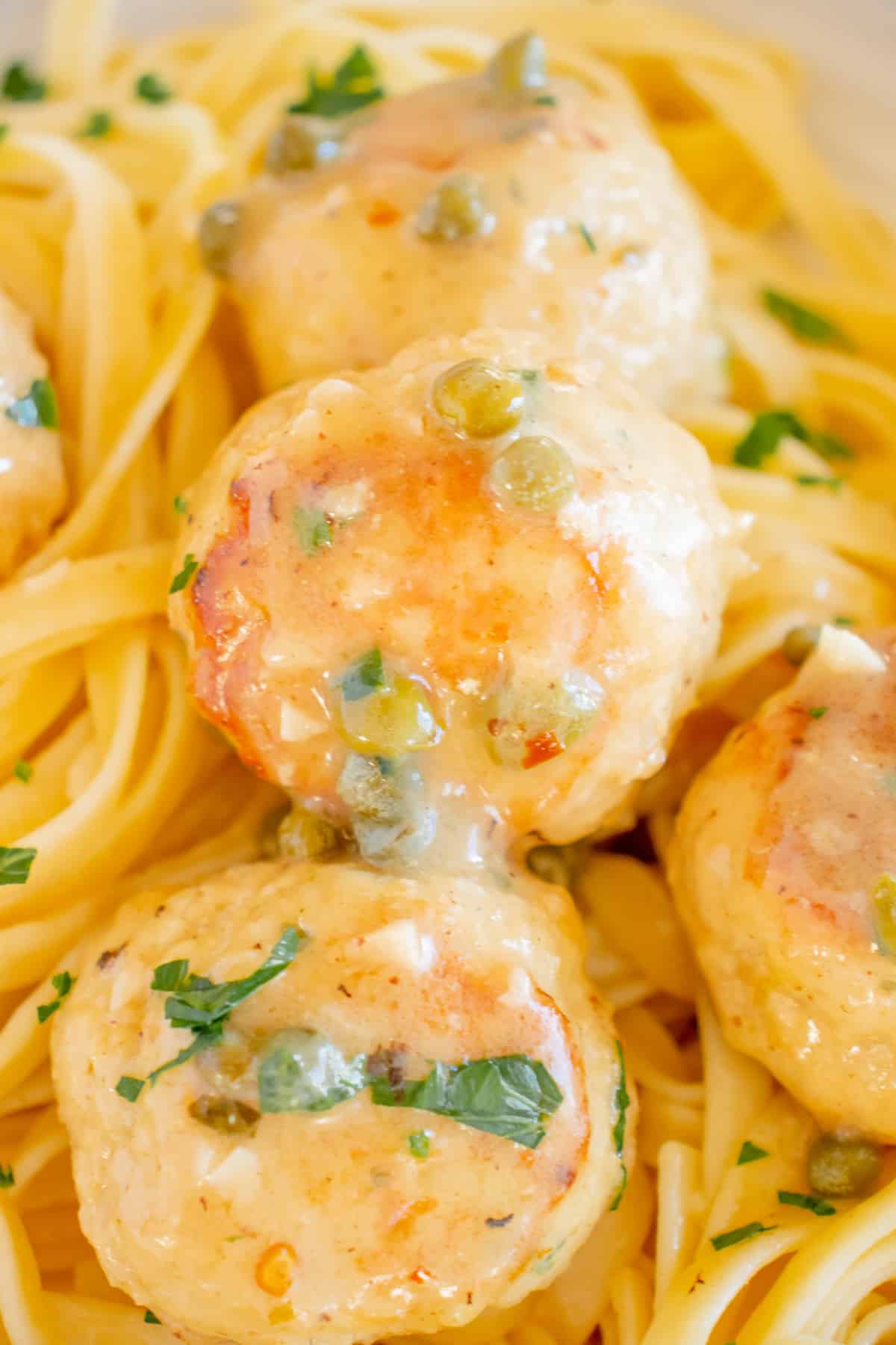 close up view of chicken piccata meatballs coated in a garlic lemon sauce with capers