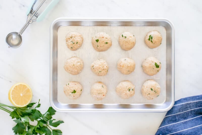 12 chicken piccata meatballs on a rimmed baking sheet.