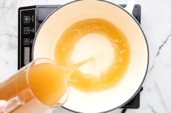 chicken broth being poured into a dutch oven.