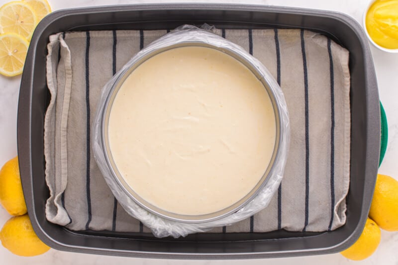 lemon meringue cheesecake batter in a springform pan wrapped in foil in a water bath.