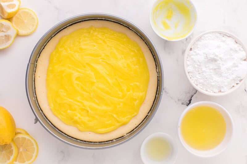 lemon curd spread over baked lemon meringue cheesecake in a springform pan.