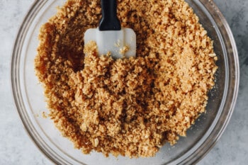 graham cracker crust for no bake cheesecake in a glass bowl with a rubber spatula.