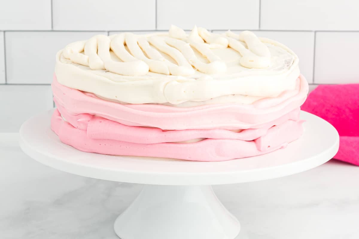 side view of ombre frosting piped around pink velvet cake on a white cake stand.