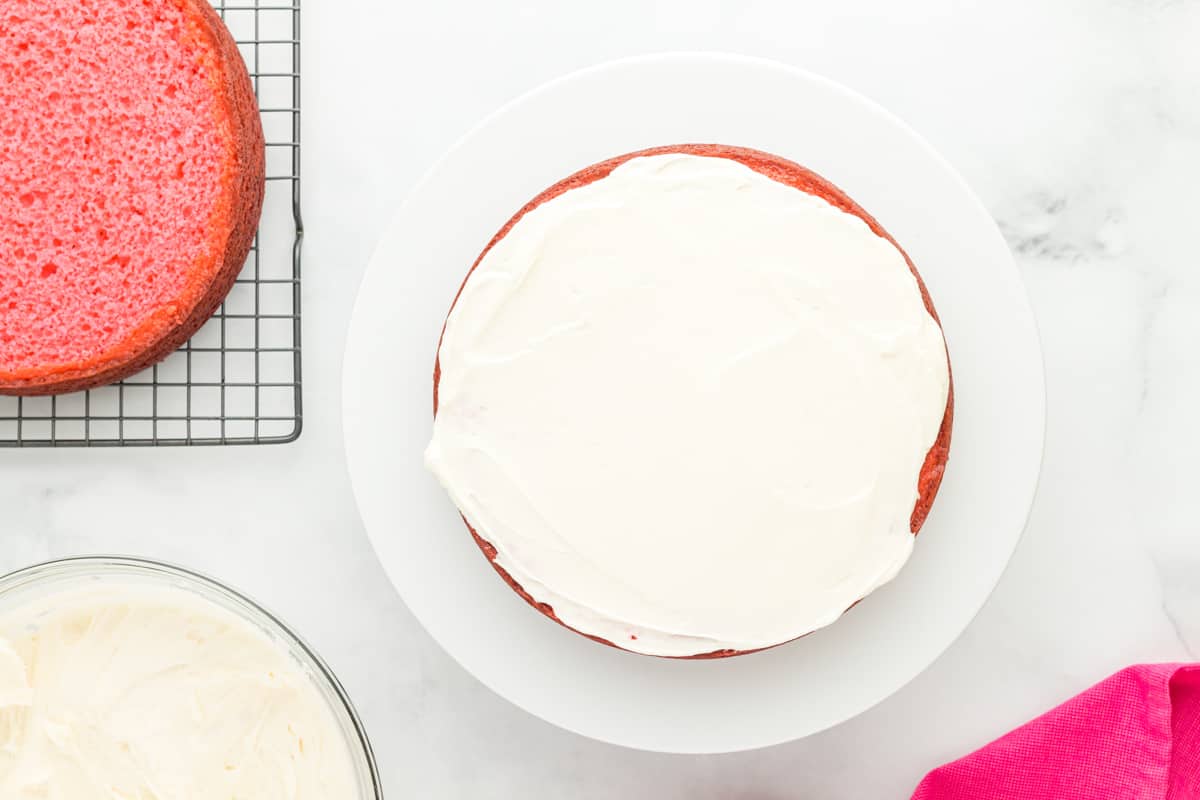 overhead view of a pink velvet cake layer covered in frosting on a white cake stand.