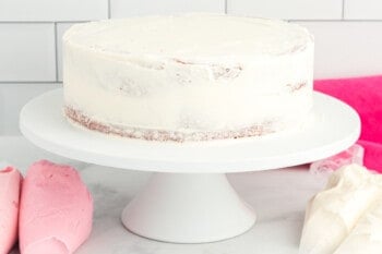 side view of a crumb coated pink velvet cake on a white cake stand.