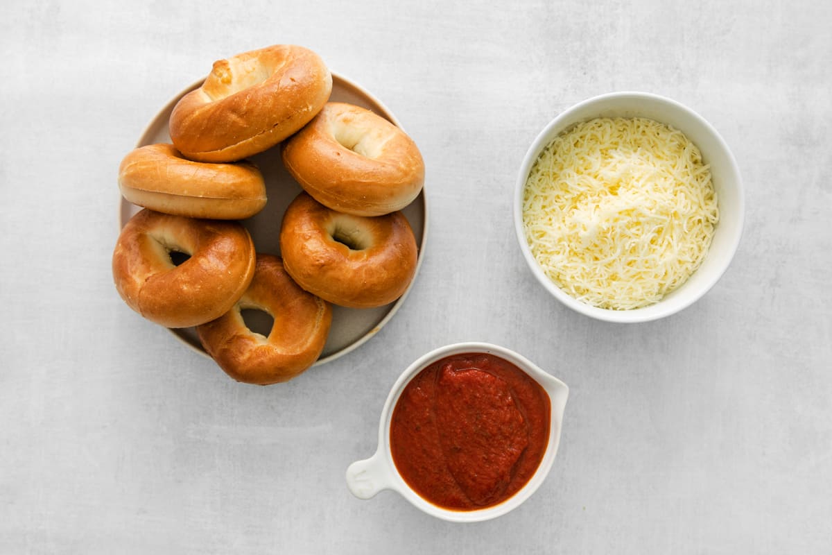 overhead view of sliced bagels, shredded cheese, and marinara sauce in individual bowls.