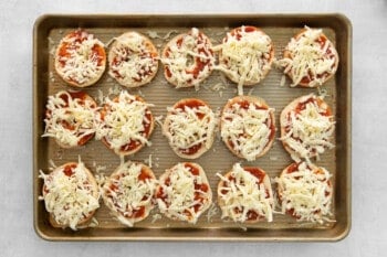 15 unbaked pizza bagels on a baking sheet.