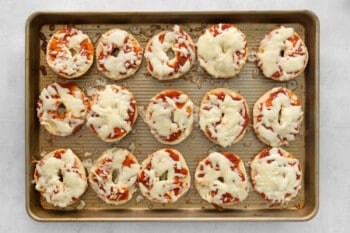 15 baked pizza bagels on a baking sheet.