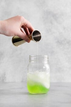 lime juice added to apple liqueur, vodka, and simple syrup in a mason jar with ice.