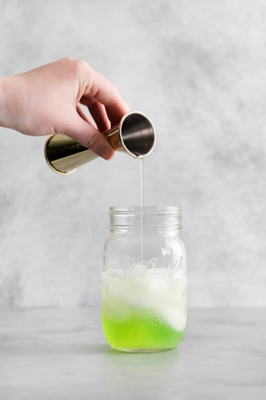 lime juice added to apple liqueur, vodka, and simple syrup in a mason jar with ice.