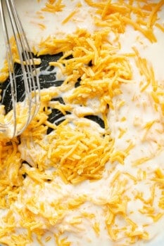 cheese added to cheese sauce base in a pan with a whisk.