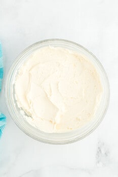 overhead view of white frosting in a glass bowl.