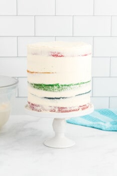 side view of a crumb coated rainbow cake on a white cake stand.