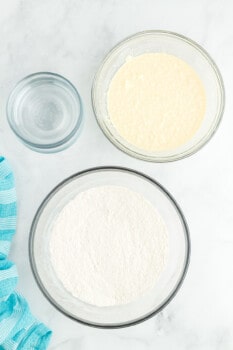 overhead view of wet and dry ingredients for rainbow cake in glass bowls.