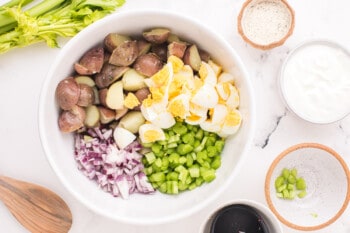 cooked potatoes, eggs, celery, and onion in a white bowl.