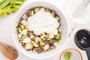 ranch dressing mixture dolloped over ranch potato salad in a white bowl.