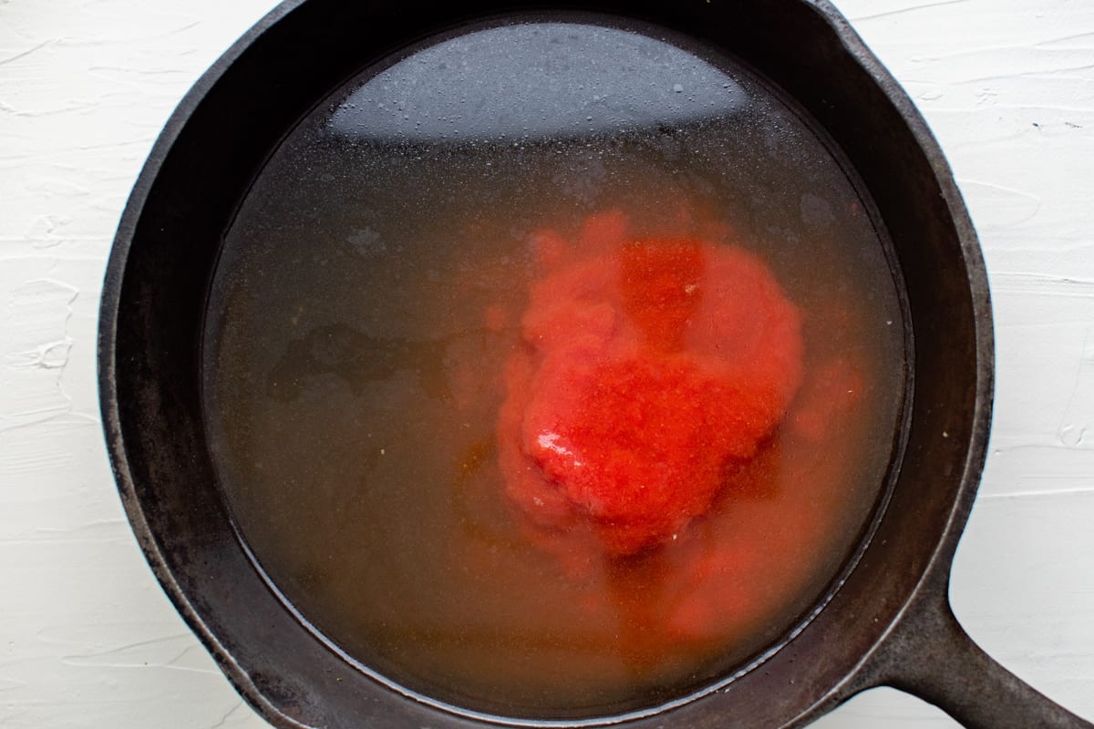 chicken broth and tomato sauce in a cast iron pan.