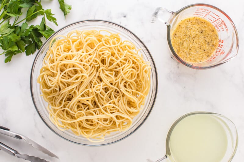 cooked spaghetti in a glass bowl with pasta cooking water and egg mixture in separate bowls.