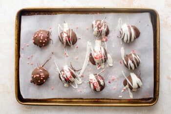 10 strawberry truffles drizzled with white chocolate and sprinkles on a baking sheet.