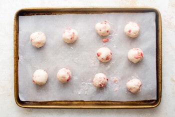 10 rolled strawberry truffles on a baking sheet.
