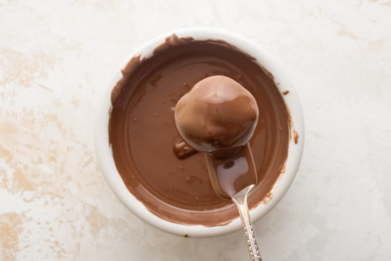 a fork suspending a chocolate coated strawberry truffle over a bowl of melted chocolate.