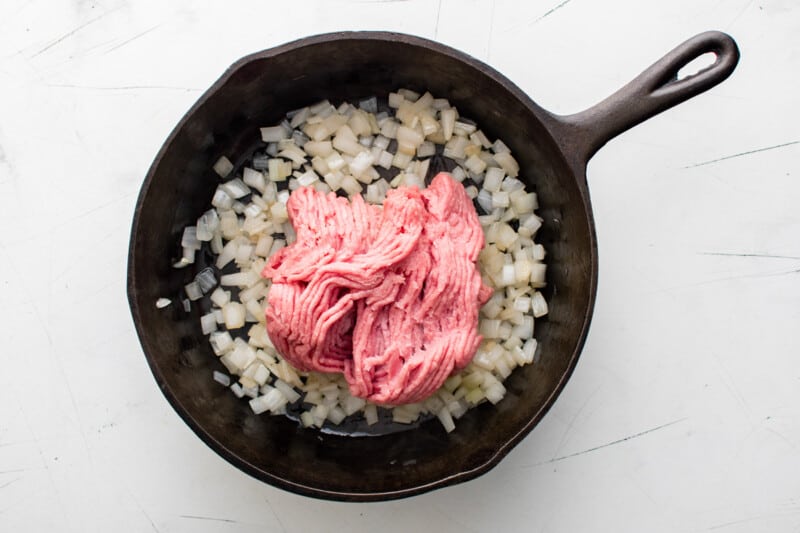 cooked onions and raw ground beef in a cast iron pan.