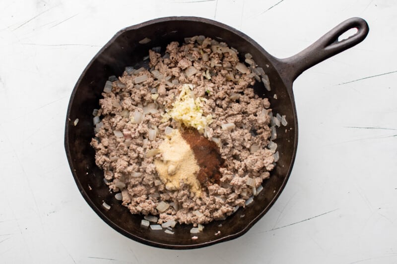 taco seasoning added to cooked ground beef and onions in a cast iron pan.