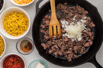 cooked ground beef and diced onion in a cast iron pan with a wooden spoon.