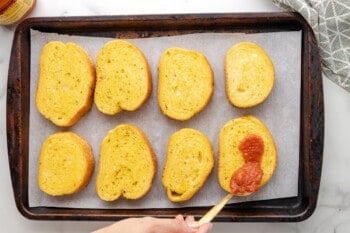 tomato sauce spooned over slices of texas toast on a baking sheet.