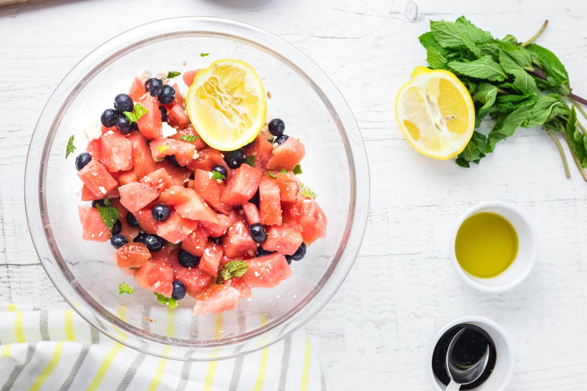watermelon salad mixed together in a glass bowl with a lemon.