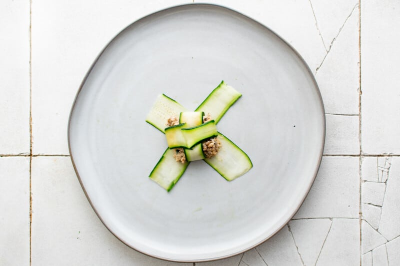zucchini ribbons folded over a dollop of filling on a white plate.